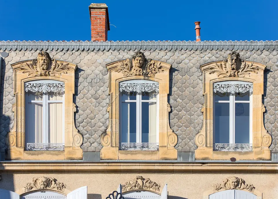 Fenêtres du dernier étage de la maison Jailles à Agen, encadrées de décors sculptés en pierre sur un mur orné d'écailles décoratives.