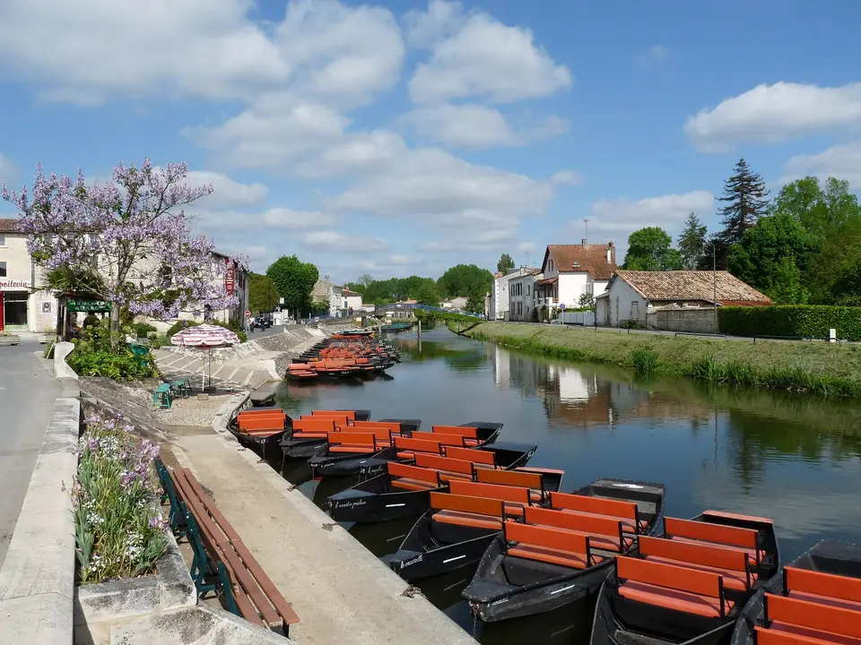 Quai Louis Tardy à Coulon, barques plates amarrées le long du canal du Marais poitevin bordé de maisons et d'arbres en fleurs.