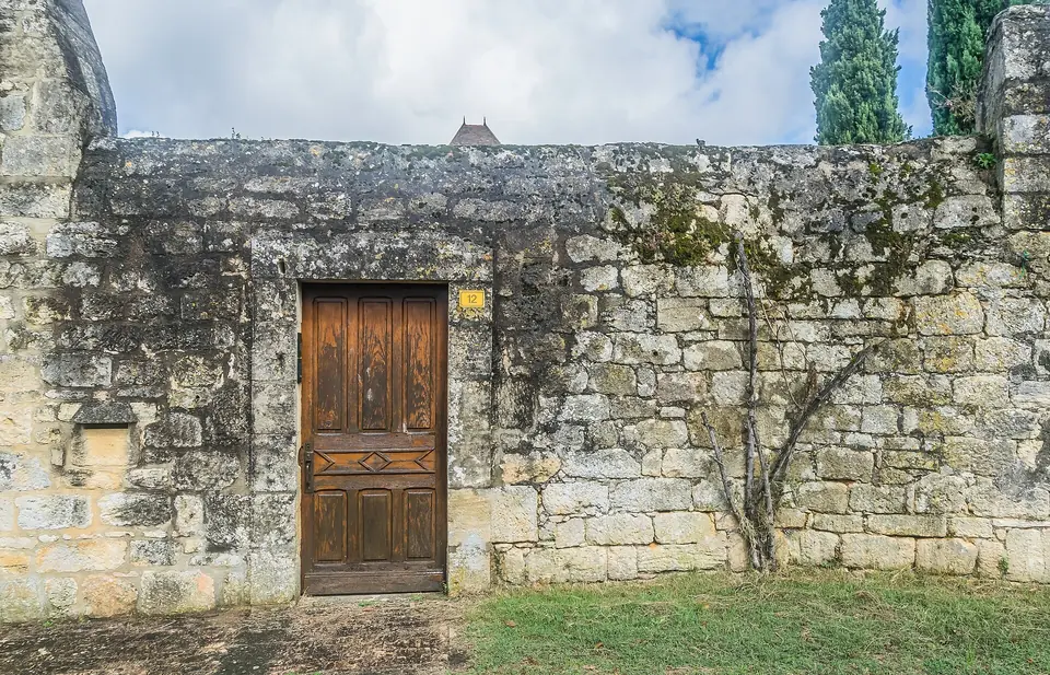 Porte en bois à panneaux moulurés dans un vieux mur de pierre à Domme, au bord d'une pelouse.